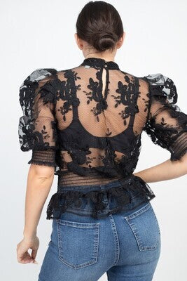 A knit top featuring sheer material, lace trim, short bubble sleeves, a mock neckline, a back keyhole closure, and a smocked waist. Made in China