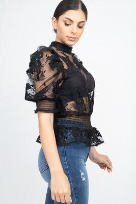 A knit top featuring sheer material, lace trim, short bubble sleeves, a mock neckline, a back keyhole closure, and a smocked waist. Made in China
